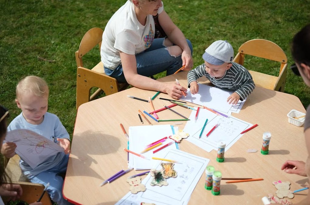 Children and parents engaging in outdoor art and craft activities with colored pencils.