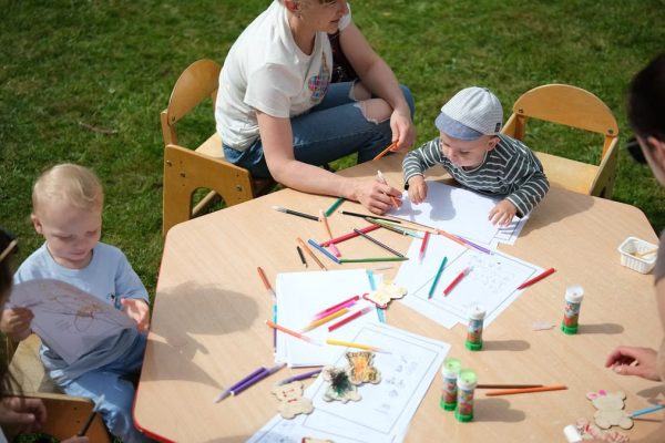Children and parents engaging in outdoor art and craft activities with colored pencils.